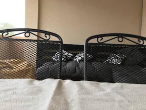 Ein Bett mit Metallgestell und weißer Bettdecke, mit Kissen in Schwarz-Weiß-Muster.