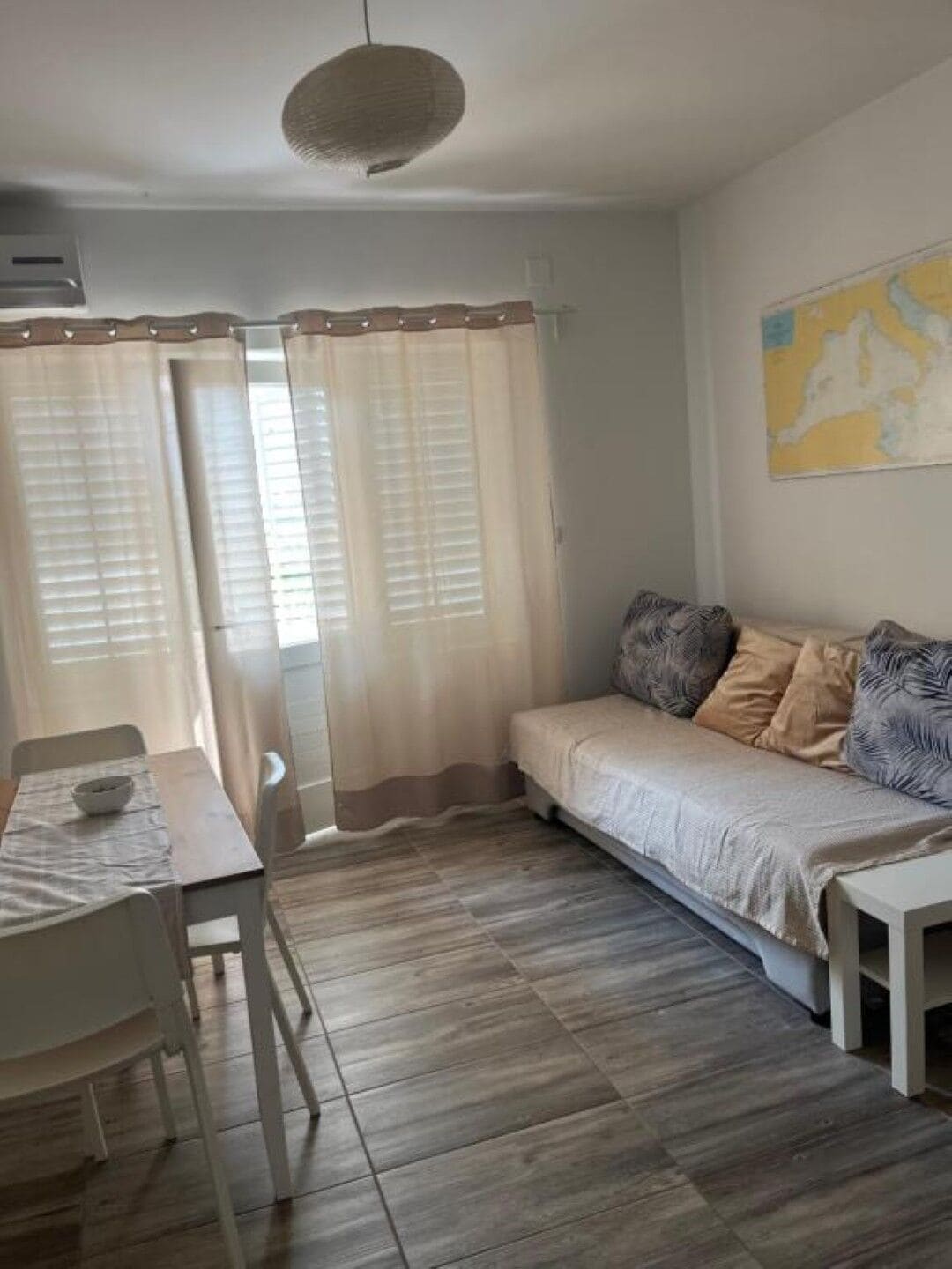 Ein gemütliches Zimmer mit Holzboden, einem Bett mit gemusterten Kissen, einem kleinen Tisch mit einer Schale und einer Karte an der Wand.