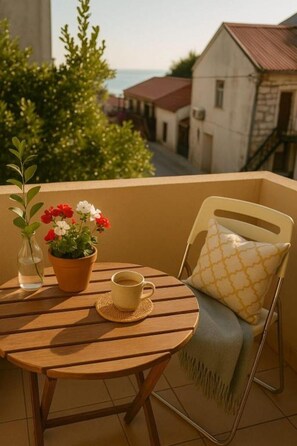 Ein runder Holztisch mit einem Blumentopf, einer Tasse und einem Stuhl mit einem gemusterten Kissen auf einem Balkon.