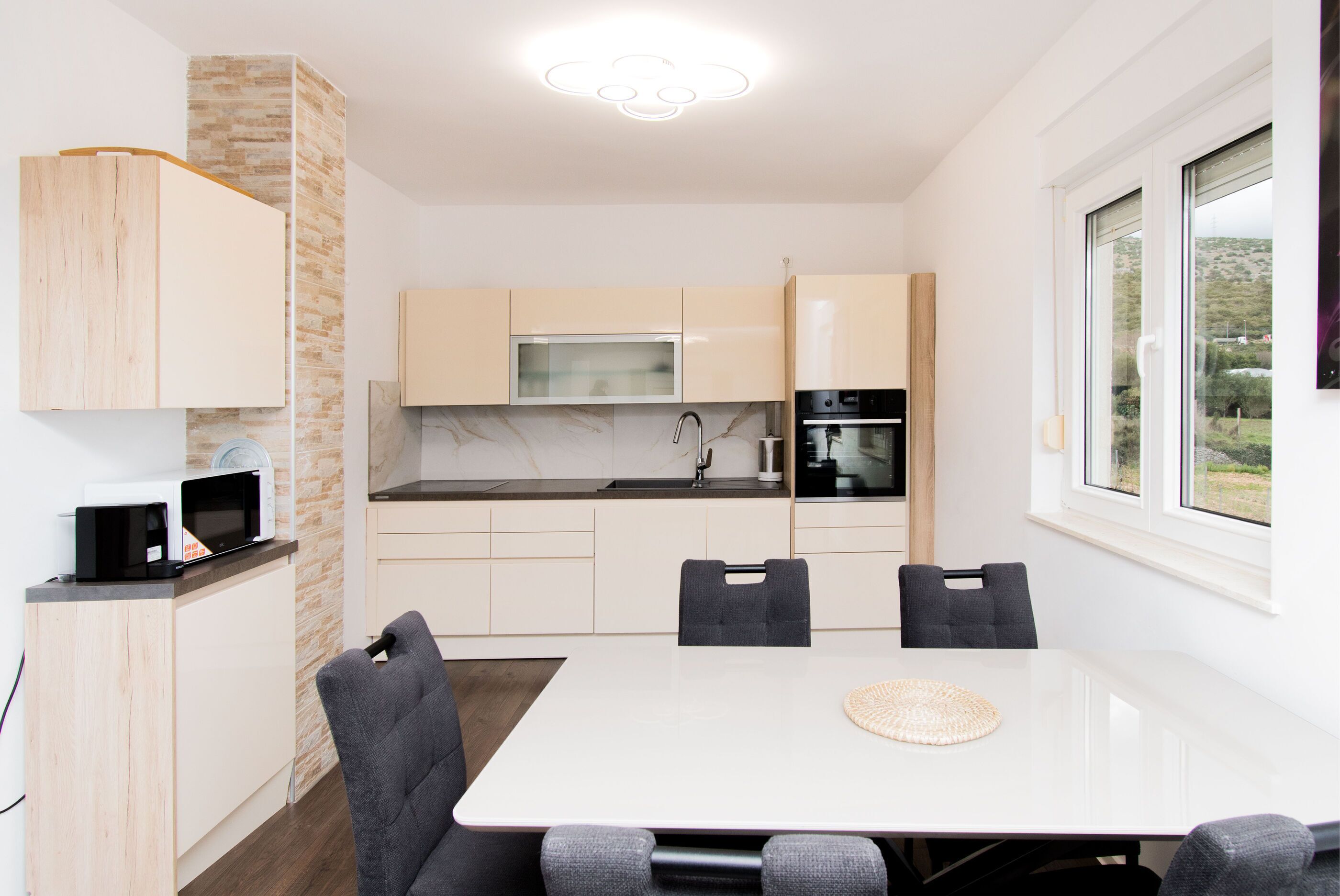 A modern kitchen with a dining area, a microwave, a coffee machine, and a view of the outdoors.