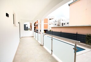 A corridor with a pool on one side, a white wall, and a building with scaffolding in the background. - Apartments Jozak (Trogir)