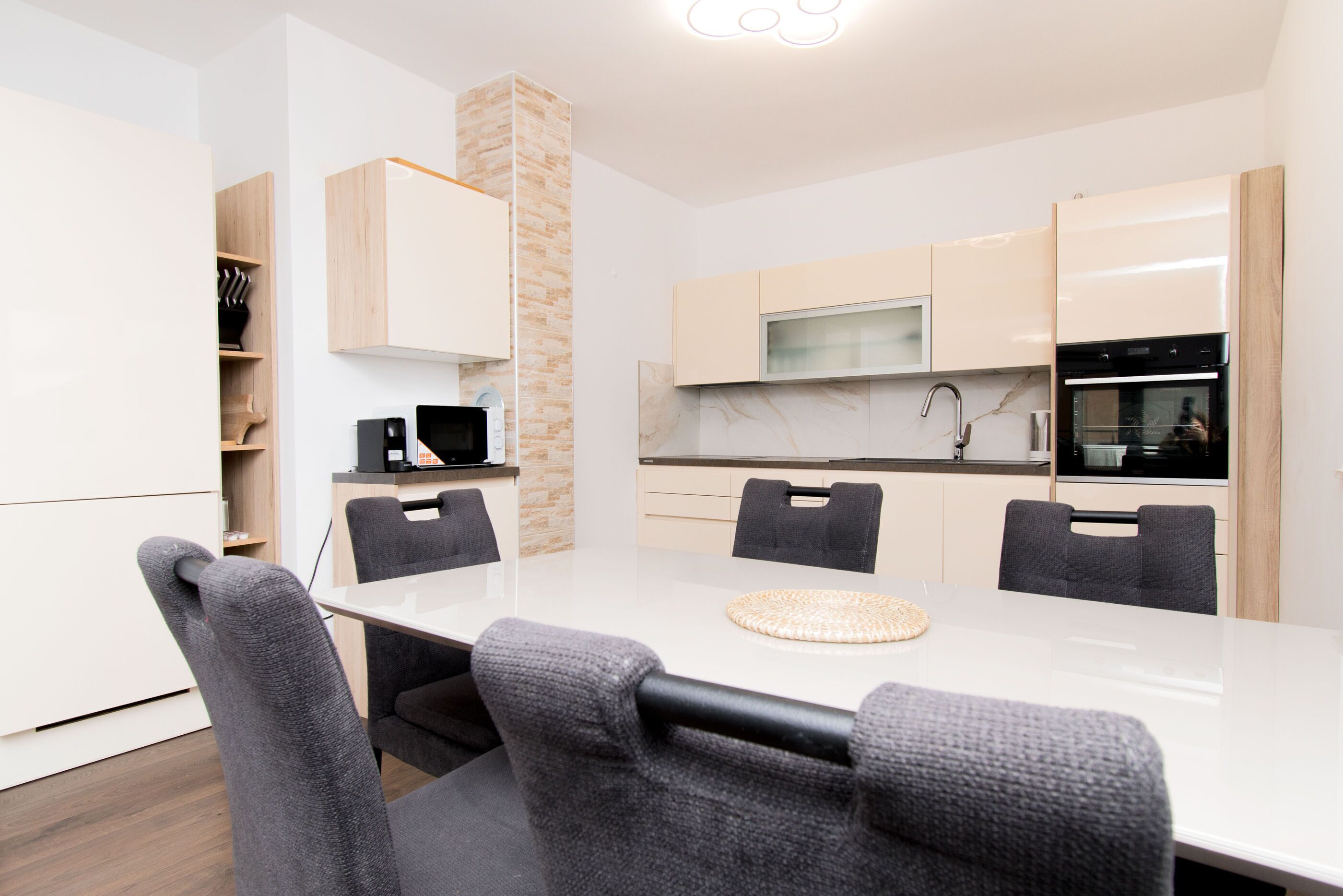 A modern kitchen with a white countertop, grey chairs, and built-in appliances.