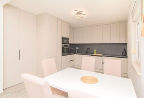 A modern kitchen with white cabinets, a black countertop, and a white dining table with pink chairs. - Apartments Jozak (Trogir)