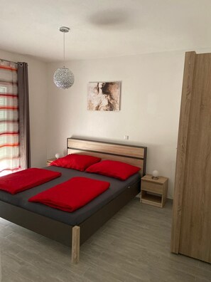 A bedroom with a bed, a bedside table, a nightstand, a hanging light fixture, and a painting on the wall. - Apartments Jozak (Trogir)