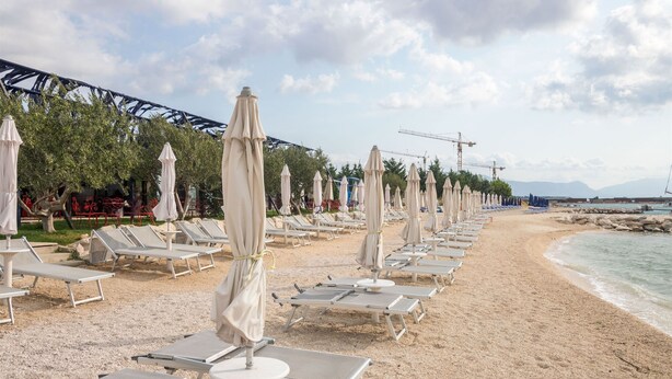 A beach with rows of sun loungers and umbrellas, a construction crane, and a clear sky. - Apartments Jozak (Trogir)