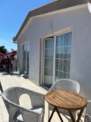 A patio with wicker chairs and a small wooden table, a sliding glass door, and a building with a light-colored exterior. - Apartments Luna Aurea (Orebic)