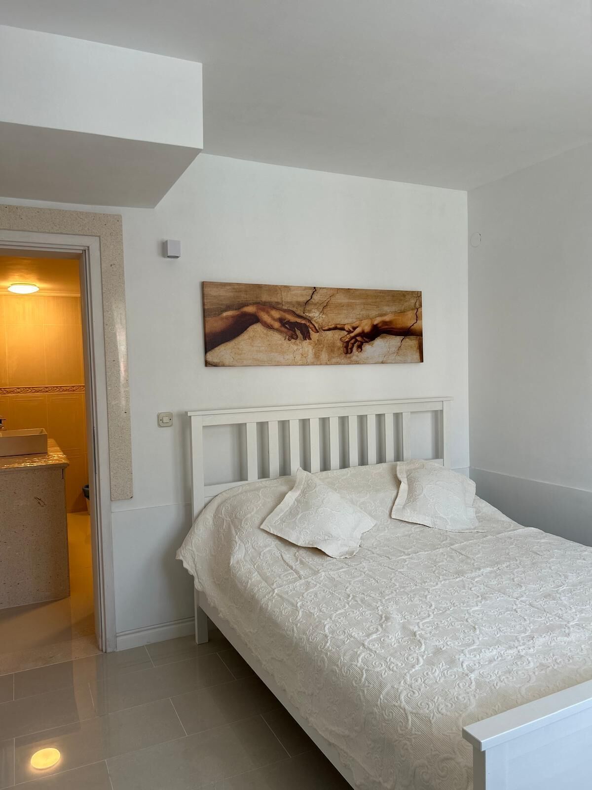 Ein Schlafzimmer mit Bett, einem Gemälde und einem durchgegangenen Tür sichtbaren Badezimmer.