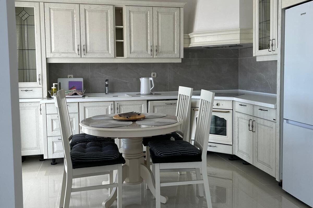 A kitchen with white cabinets, a dining table with chairs, and a refrigerator.