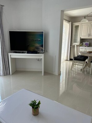 A modern living room with a flat-screen TV, a dining area with a table and chairs, and a kitchen with white cabinets. - Apartments Luna Aurea (Orebic)