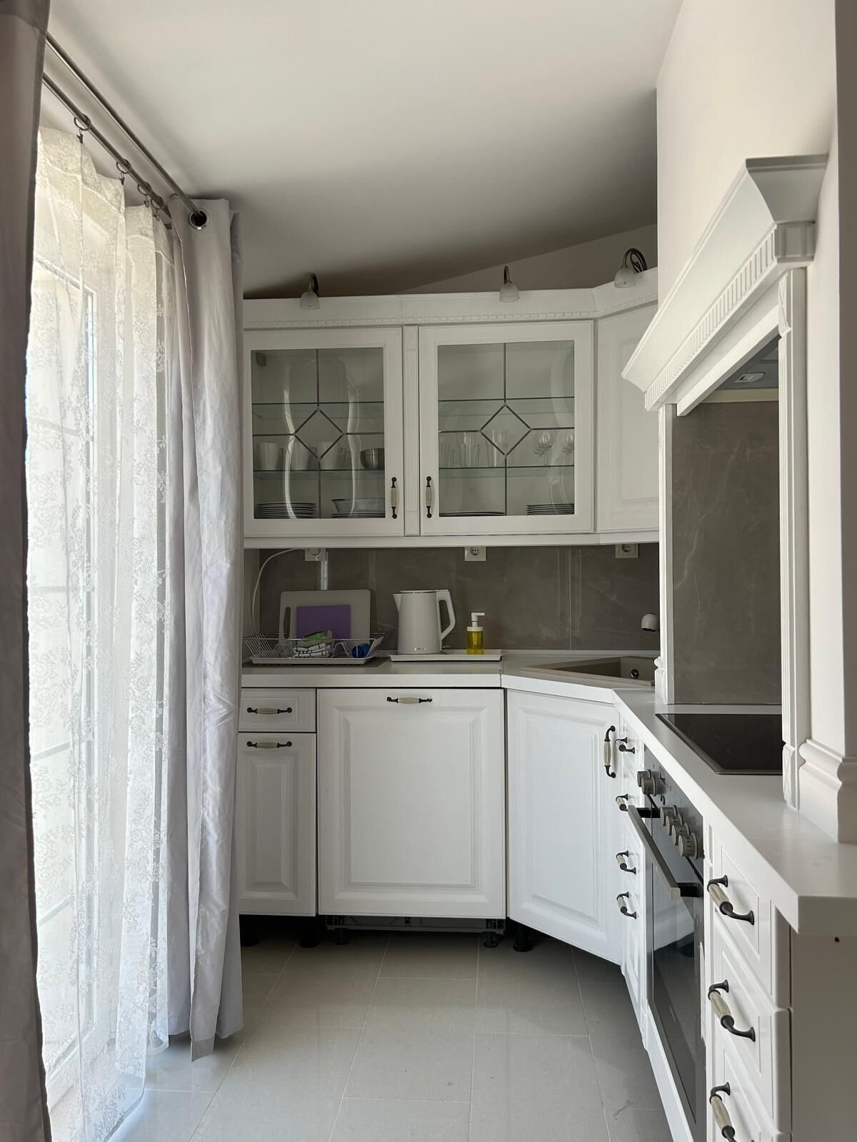 A kitchen with white cabinets, a stove, and a window with curtains.
