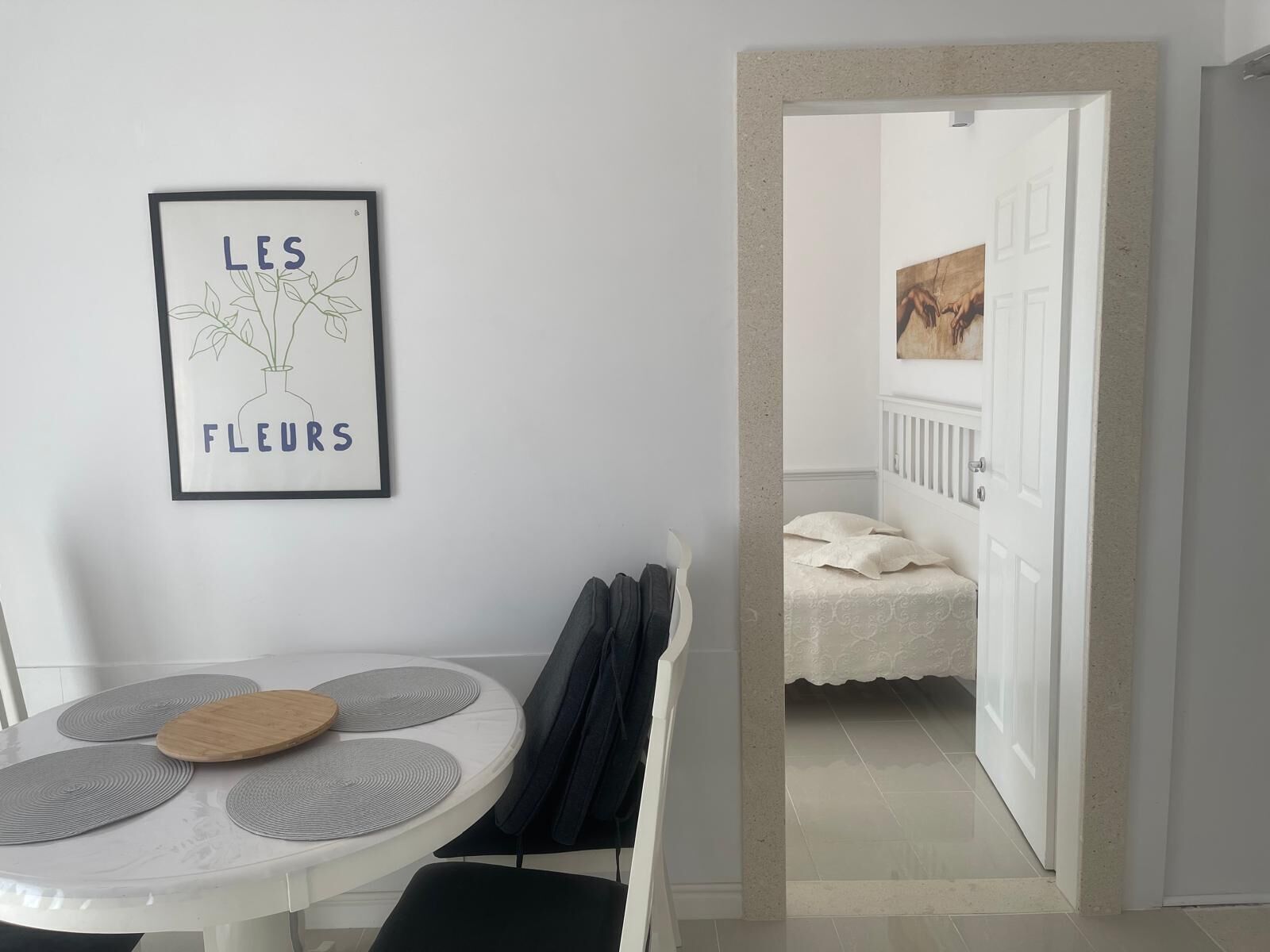 Een kamer met een witte tafel, een kunstwerk in een lijst met tekst, en een doorgang naar een andere kamer.