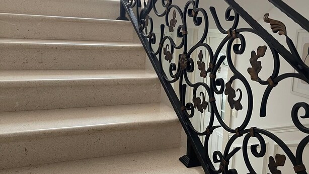 Eine Treppe mit schwarzer schmiedeeiserner Geländer und beigen Stufen.