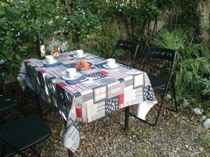 Ein Tisch im Freien, gedeckt mit einer Tischdecke, Tellern, Tassen und einer Obstschale.
