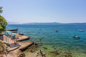 A coastal area with clear waters, steps leading down to the beach, and several boats on the water. - Apartment Nikica (Crikvenica)
