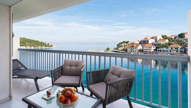 A balcony with wicker chairs and a glass table, overlooking a coastal town and turquoise waters. - Apartments Seafront Paradise (Stomorska)
