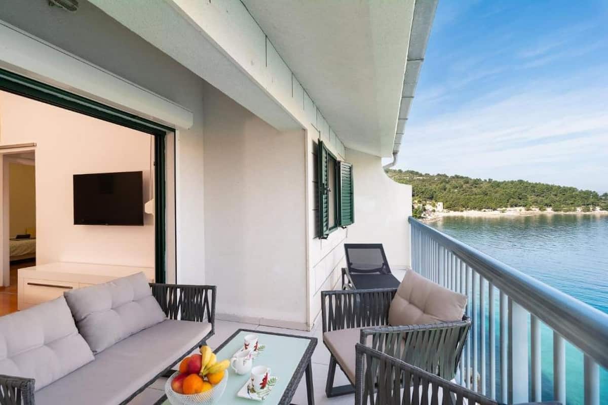A balcony with a sofa and chairs, a table with fruit and cups, and a TV on the wall.