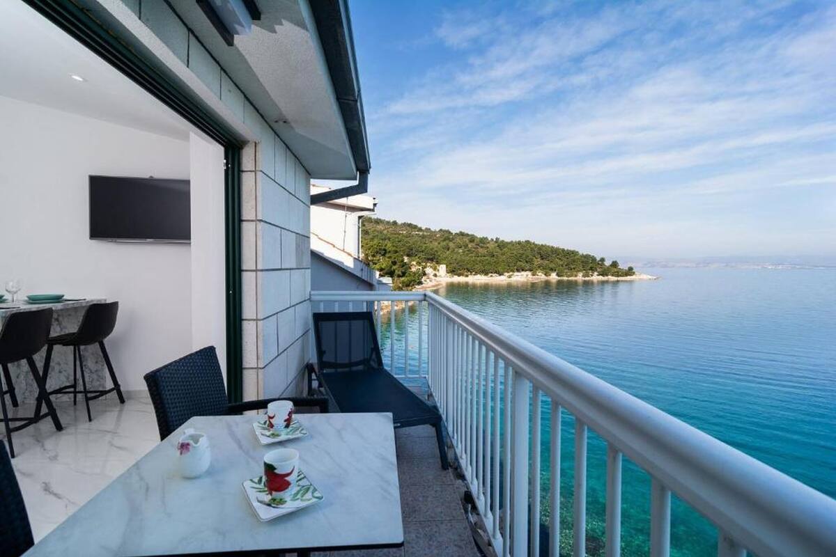 A balcony with a table set for two, overlooking a calm sea and a distant shoreline.