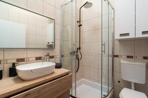 Un baño moderno con ducha envuelta en vidrio, un lavamanos blanco y un inodoro.