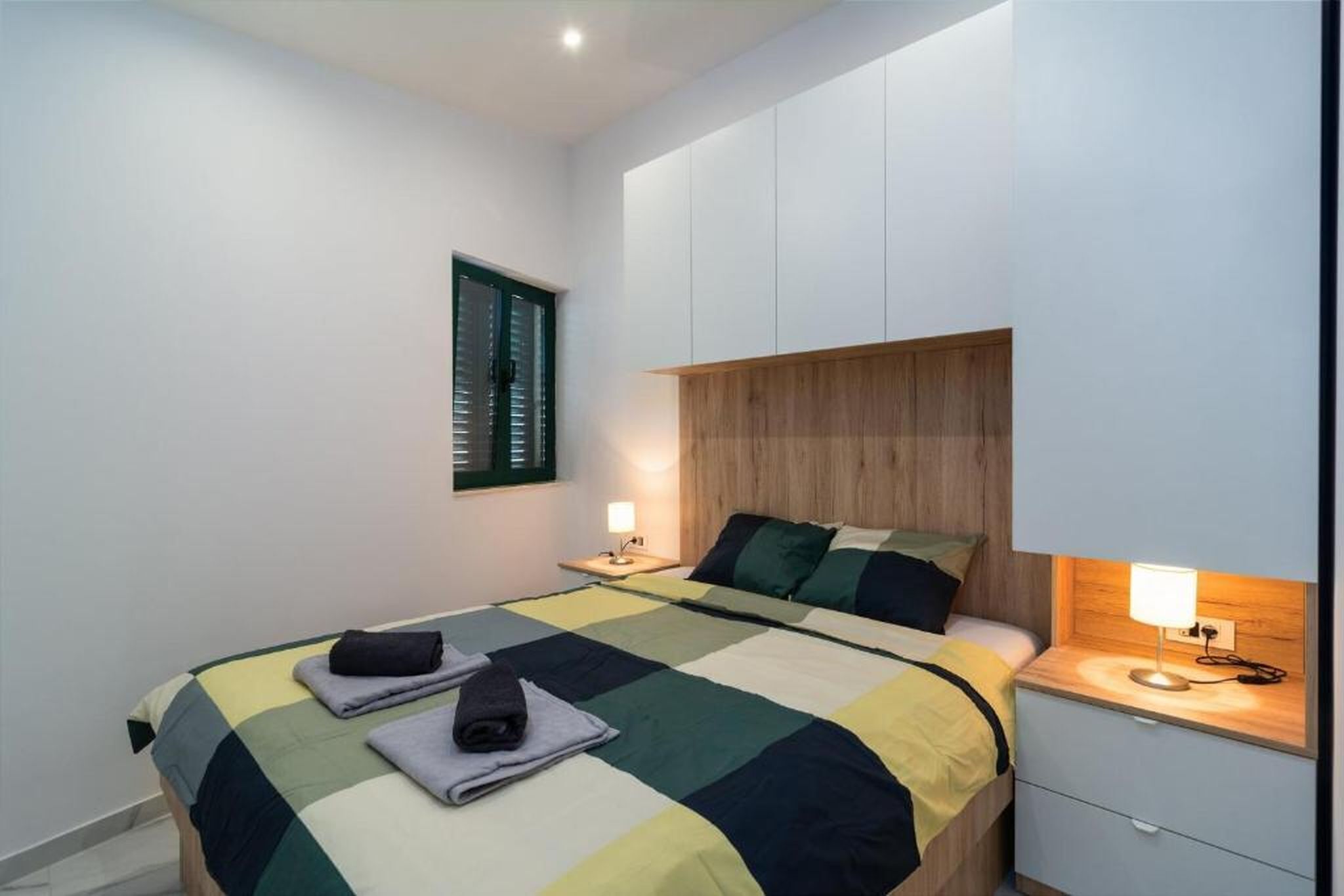 Un dormitorio moderno con una cama grande, un cabecero de madera y una mesita de noche con una lámpara.