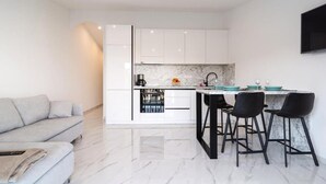 A modern kitchen with white cabinets, a marble countertop, and black bar stools. - Apartments Seafront Paradise (Stomorska)