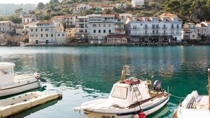 A coastal town with a row of stone buildings, a marina with boats, and a hill with vegetation in the background. - Apartments Seafront Paradise (Stomorska)