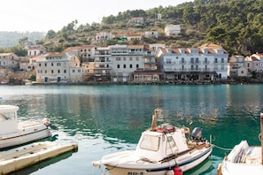 A coastal town with a row of stone buildings, a marina with boats, and a hill with vegetation in the background. - Apartments Seafront Paradise (Stomorska)