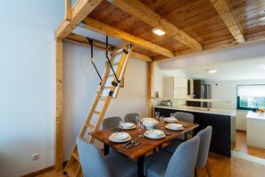 A dining area with a wooden table set for four, a ladder against the wall, and a kitchen in the background. - Apartments Seafront Paradise (Stomorska)