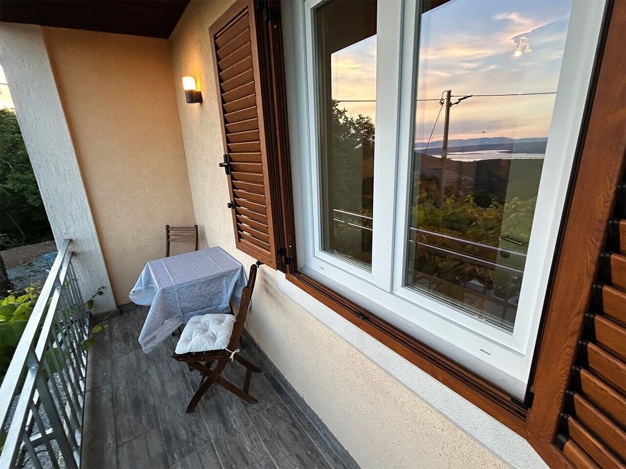Varanda com mesa e cadeira, janela com persianas e vista para o exterior.