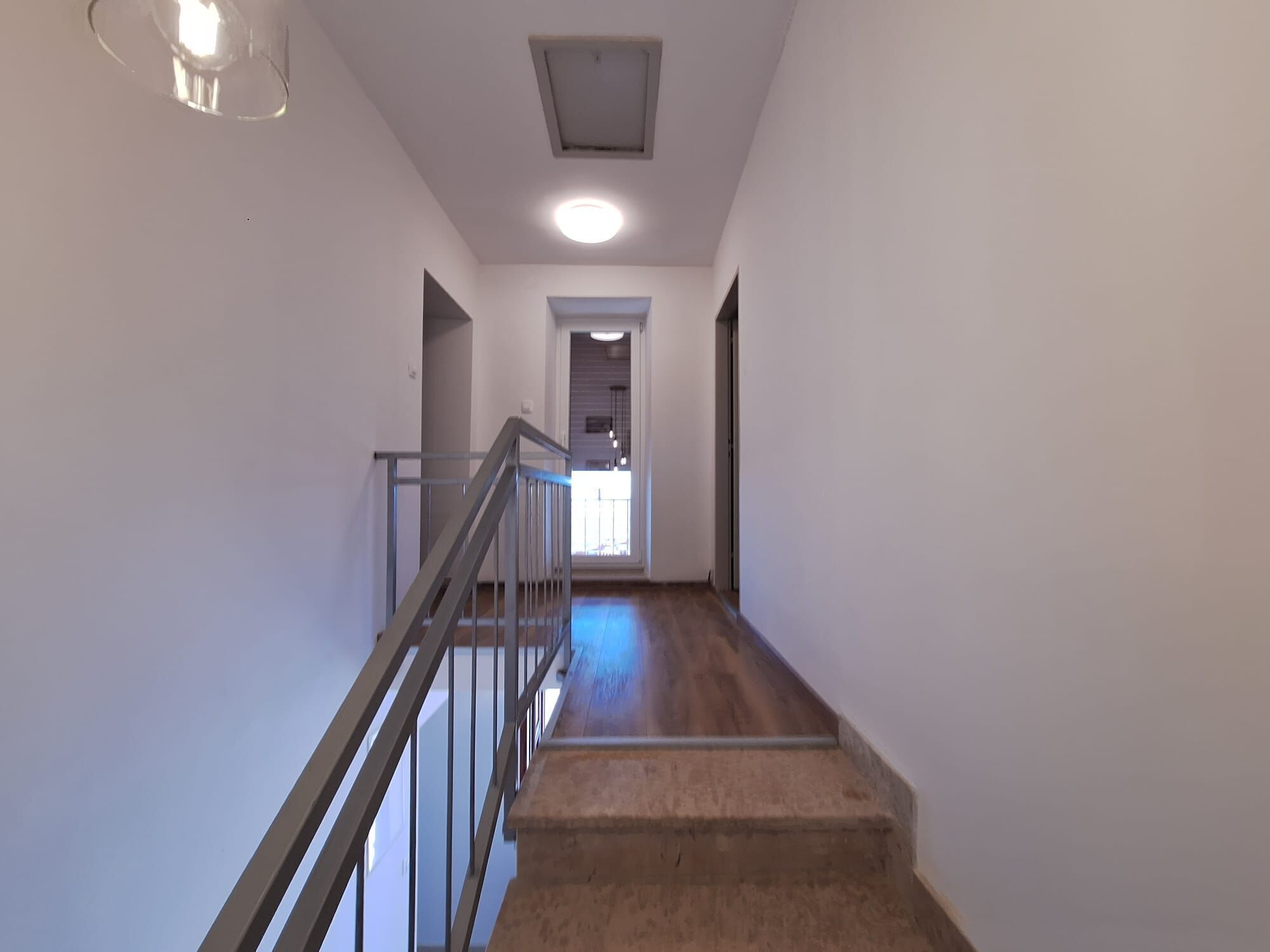 Ein Flur mit einer Treppe, die zu einer oberen Etage führt. Die Wände sind schlicht weiß gestrichen, und es gibt eine Deckenleuchte.