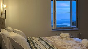 A bedroom with a bed, pillows, a bedside table, a lamp, and a window with a view of the sea. - House Martin (Vinodol)
