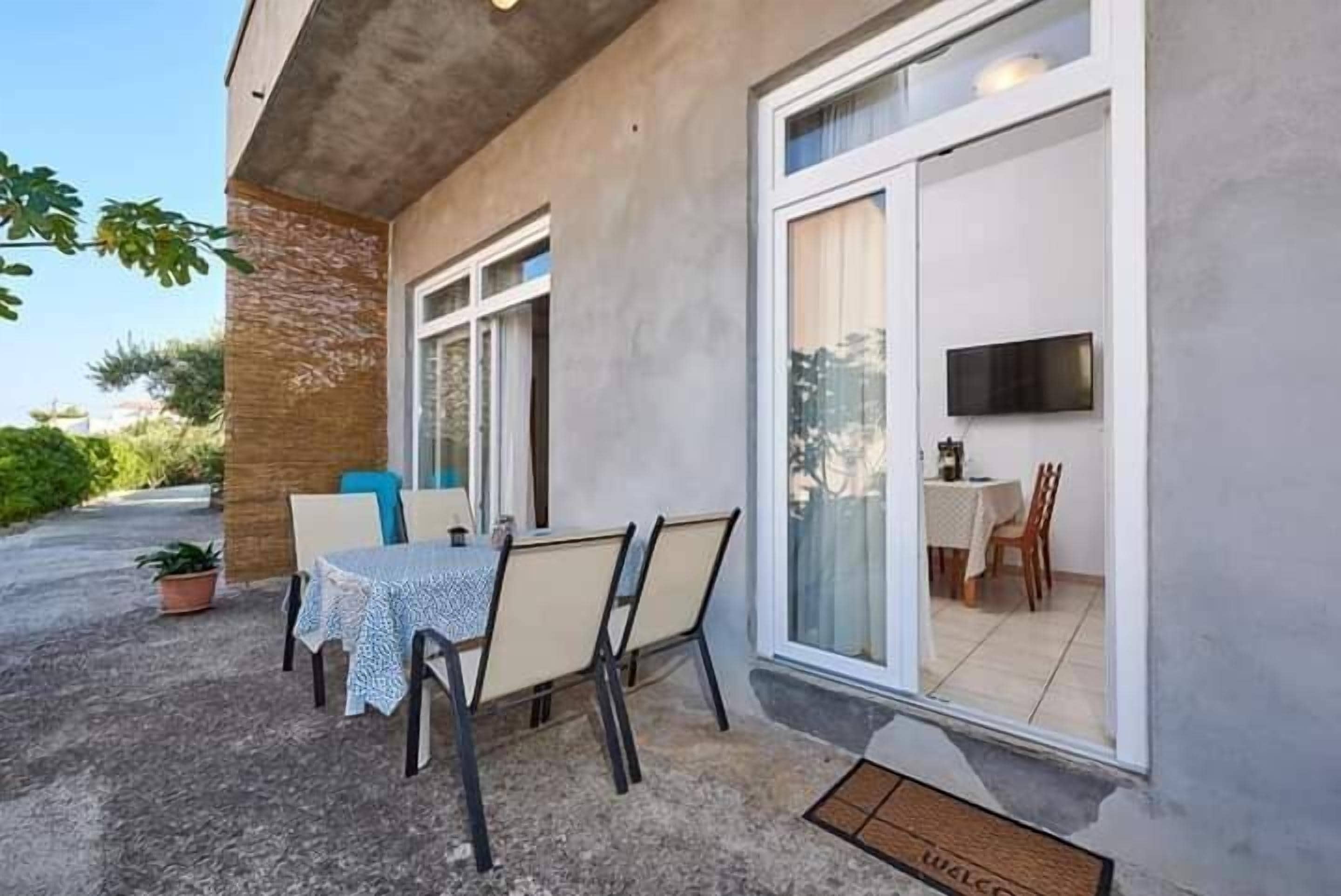Eine Terrasse im Freien mit Tisch und Stühlen, einem Topfpflanzen und einer Schiebetür zu einem Innenbereich mit Essbereich.
