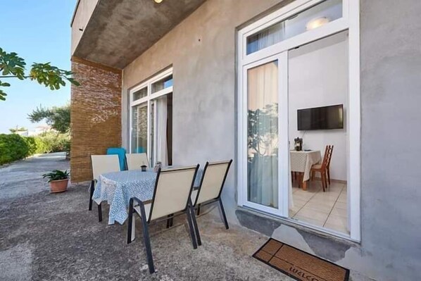 An outdoor patio with a table and chairs, a potted plant, and a sliding glass door leading to an indoor dining area. - Apartments Ornela (Split)