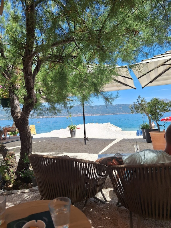Ein Sitzbereich im Freien mit Korbstühlen, einem Tisch und Blick auf das Meer und die Berge.