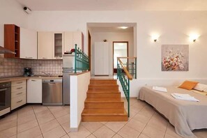 A modern kitchen with a dishwasher, a stove, and a sink. There is a staircase leading to a bedroom with a bed and a painting on the wall. - Apartments Ornela (Split)