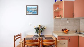 A dining table with chairs, a vase with flowers, a framed picture on the wall, and a kitchen area with cabinets and a fruit bowl. - Apartments Villa Sarajevo (Vodice)