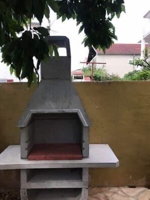 Ein grauer Grill aus Beton mit einer flachen Grillfläche und einem Schornstein, stehend auf einer weißen Plattform.