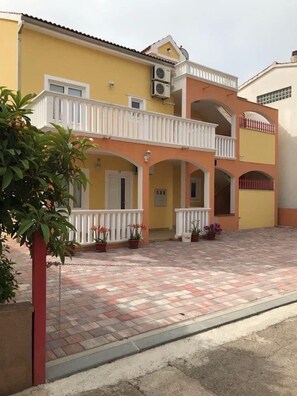 A two-story building with a yellow facade, white balconies, and a paved courtyard. - Apartments Villa Sarajevo (Vodice)