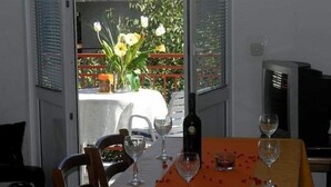 A dining table with chairs, a bottle of wine, and glasses, set against a window with a view of a garden. - Apartments Villa Sarajevo (Vodice)