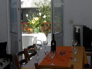 A dining table with chairs, a bottle of wine, and glasses, set against a window with a view of a garden. - Apartments Villa Sarajevo (Vodice)