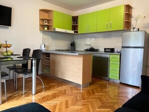 Eine kleine Küche mit grünen Schränken, einer fest eingebauten Kochinsel, einem Kühlschrank und einem Essbereich mit Stühlen.
