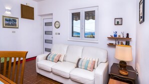 A white leather sofa with striped cushions, a wooden chair, a small table with a lamp, a clock, and a window with a view. - House Holiday House (Okrug)
