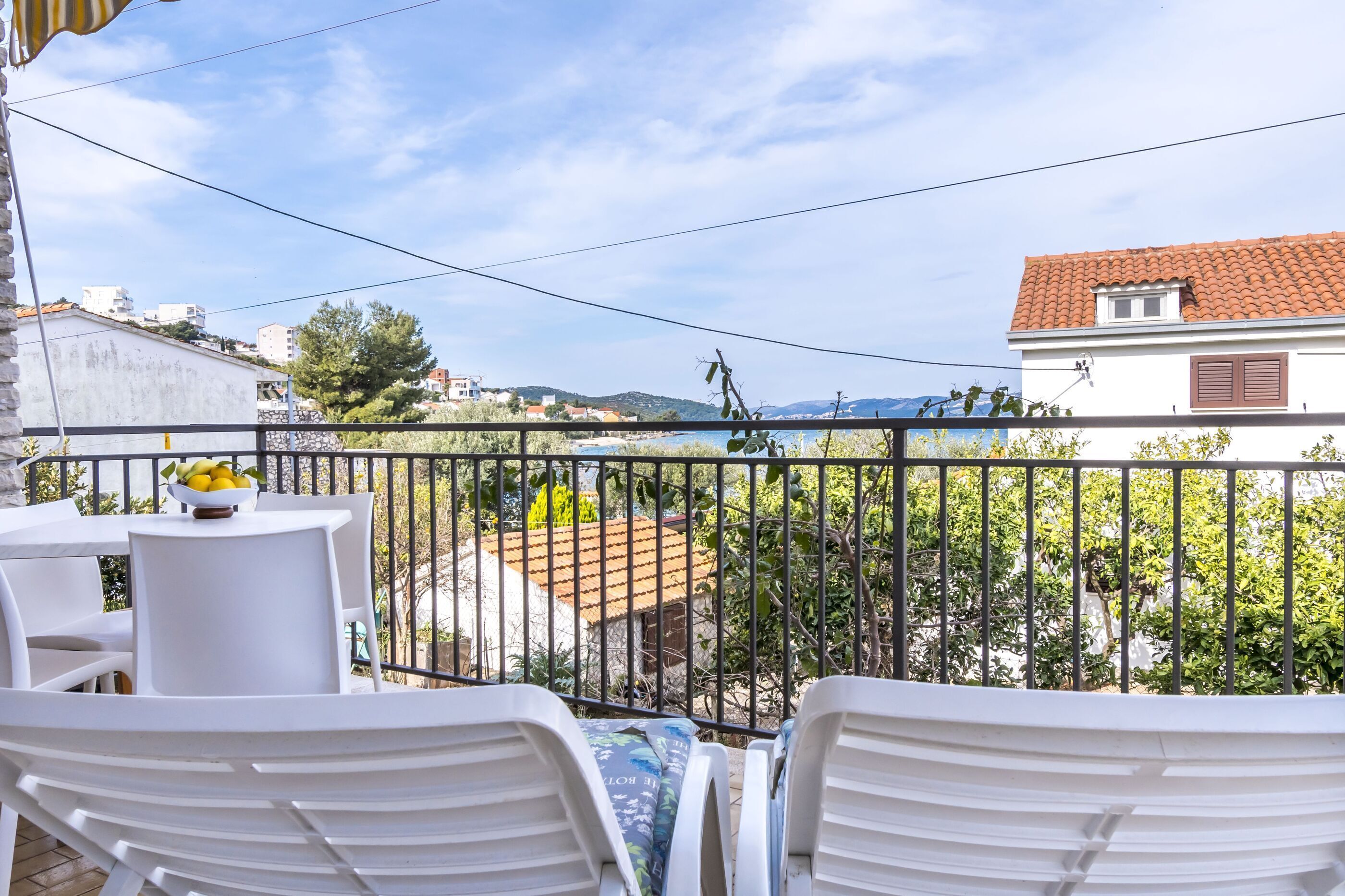 A balcony with white chairs and a table, a railing, and a view of buildings and trees.