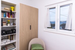 Ein Zimmer mit Bücherregal, Holzschrank, Fenster mit Aussicht und Sessel mit Kissen.