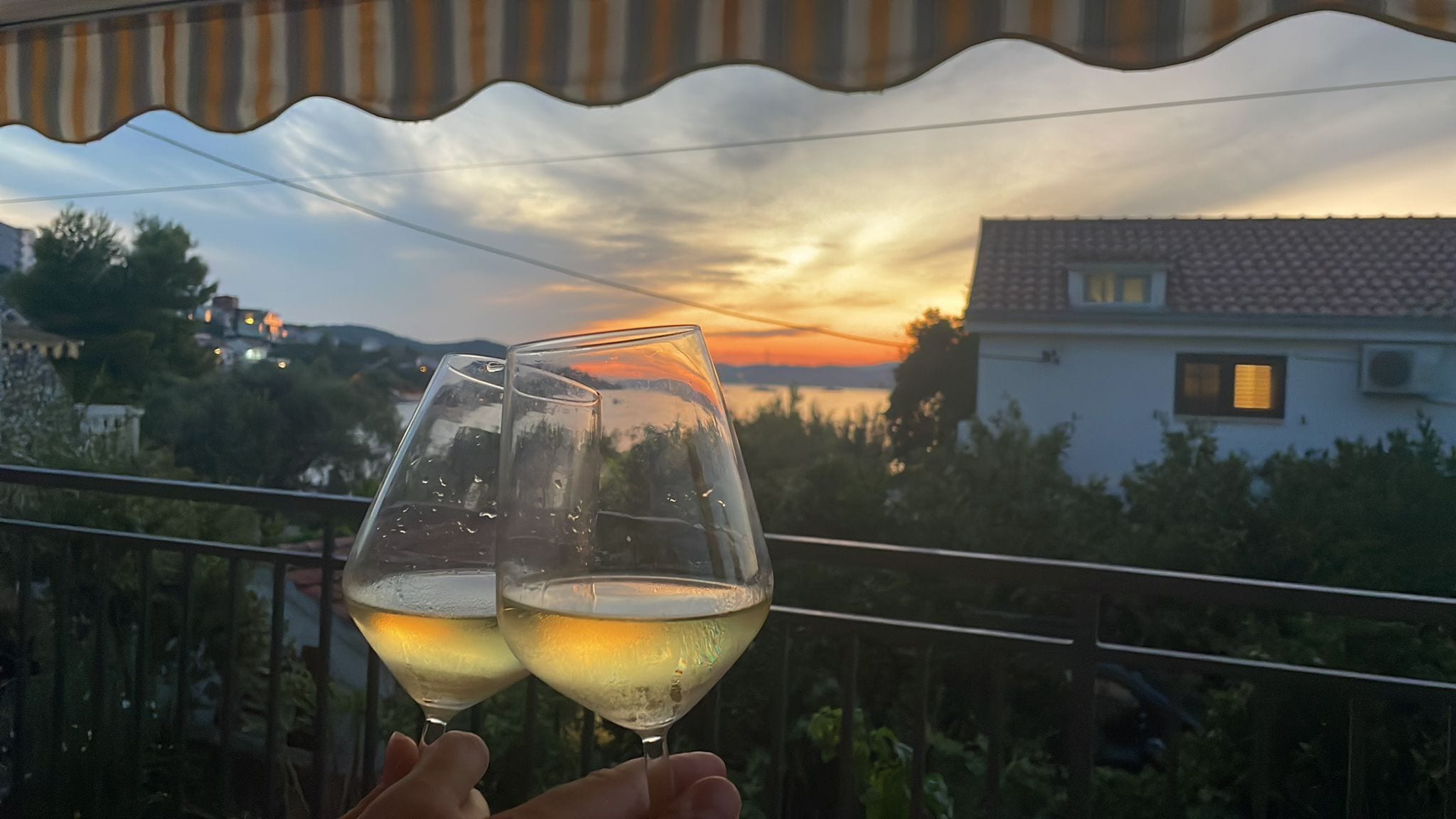 Two glasses of white wine on a balcony with a sunset view.