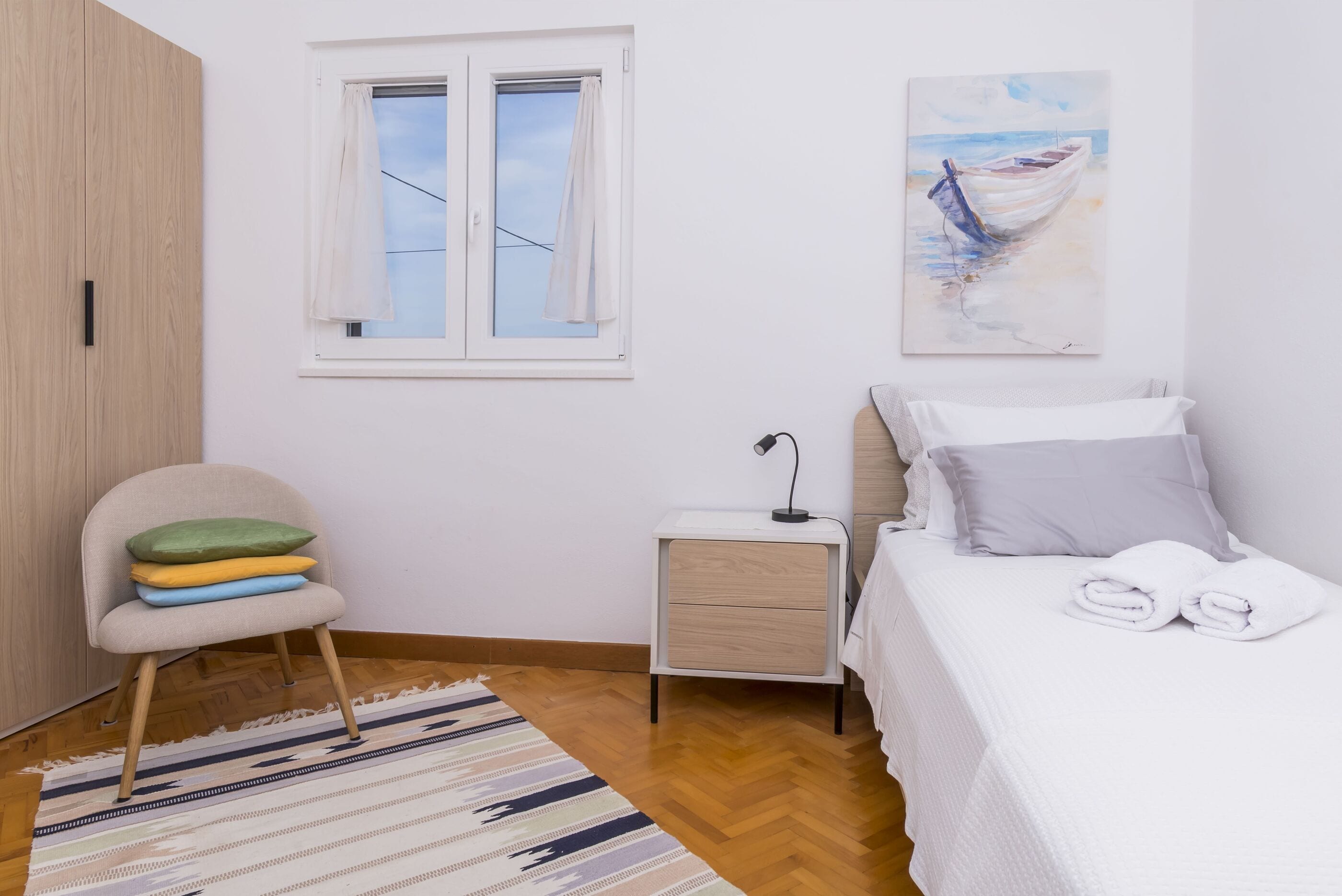 Une chambre à coucher avec un lit, une table de chevet, une chaise, une fenêtre et un tableau au mur.