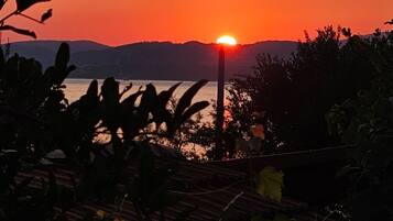 A sunset over a body of water with silhouettes of trees and a distant mountain range.