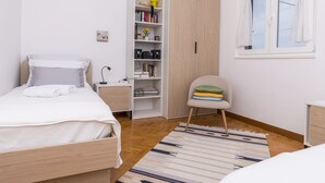 Un dormitorio con cama, mesita de noche, armario, silla y ventana.