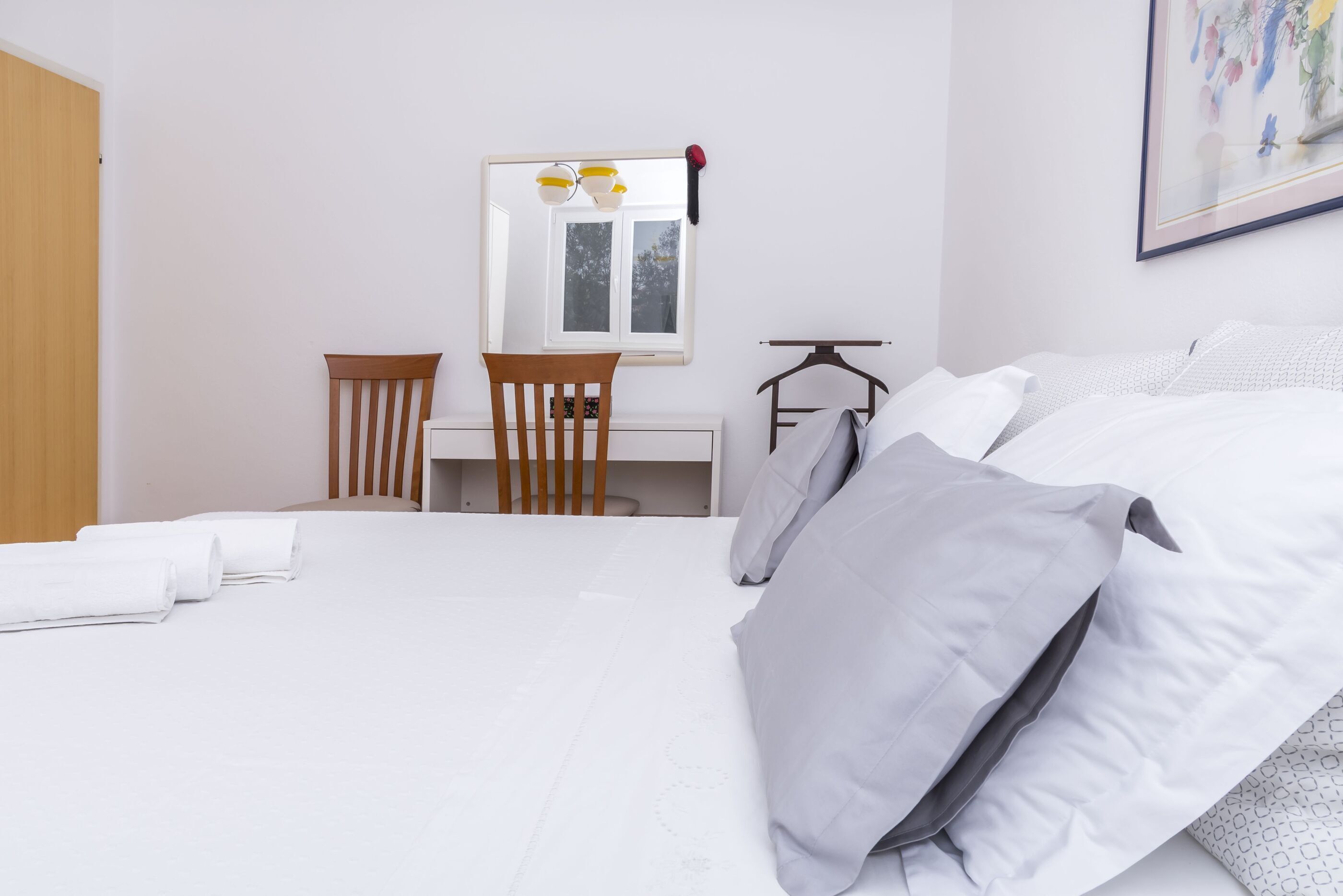 Un dormitorio con cama, una silla, un escritorio, una lámpara colgante y una ventana.