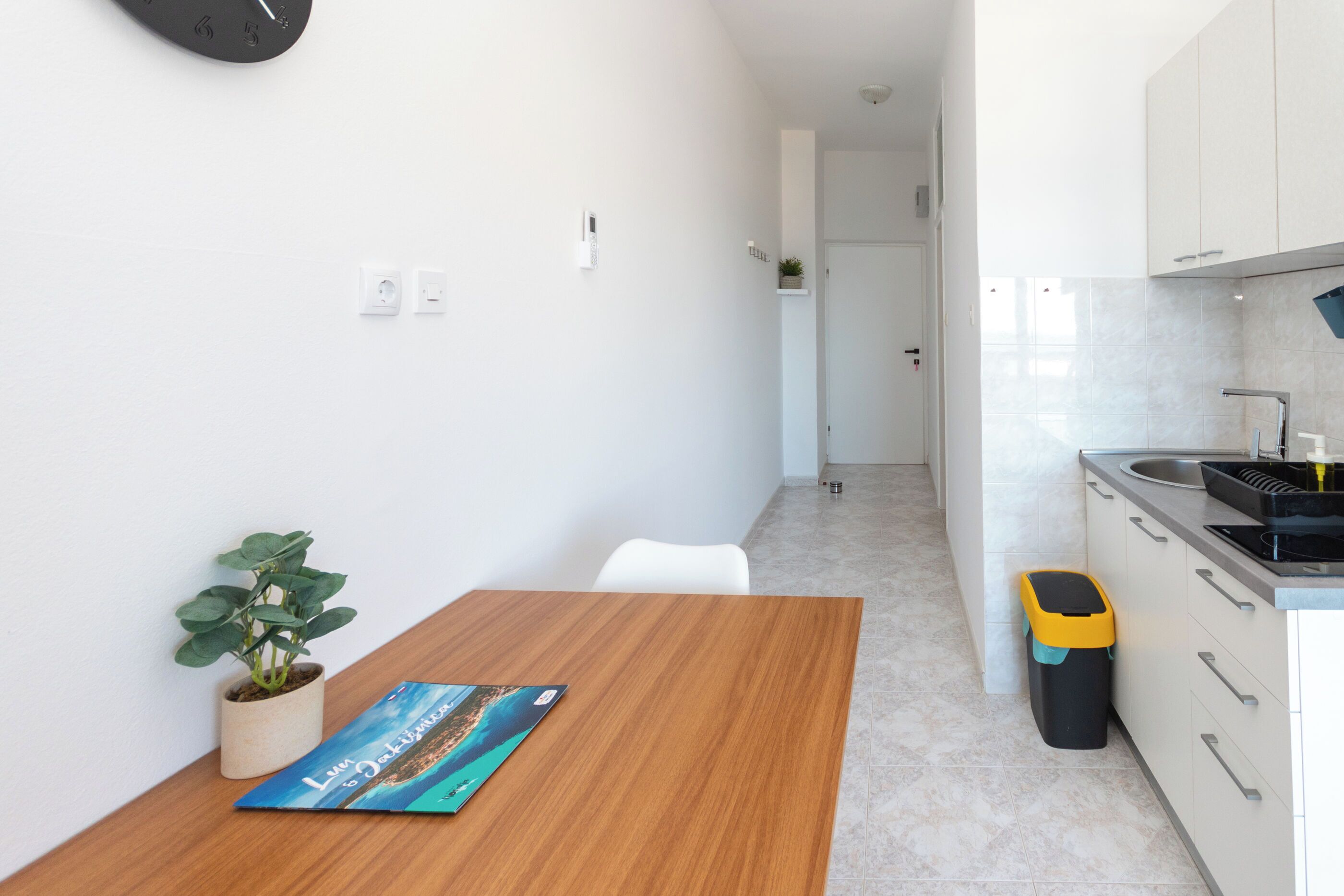 A modern kitchen with white cabinets, a wooden table, and a potted plant.