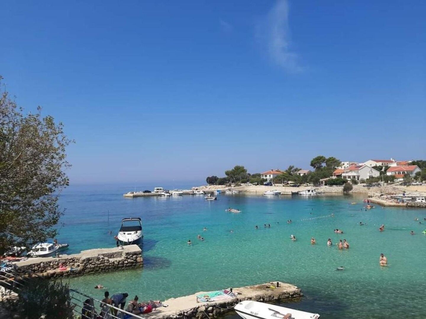 A coastal area with clear blue water, boats, and people swimming.